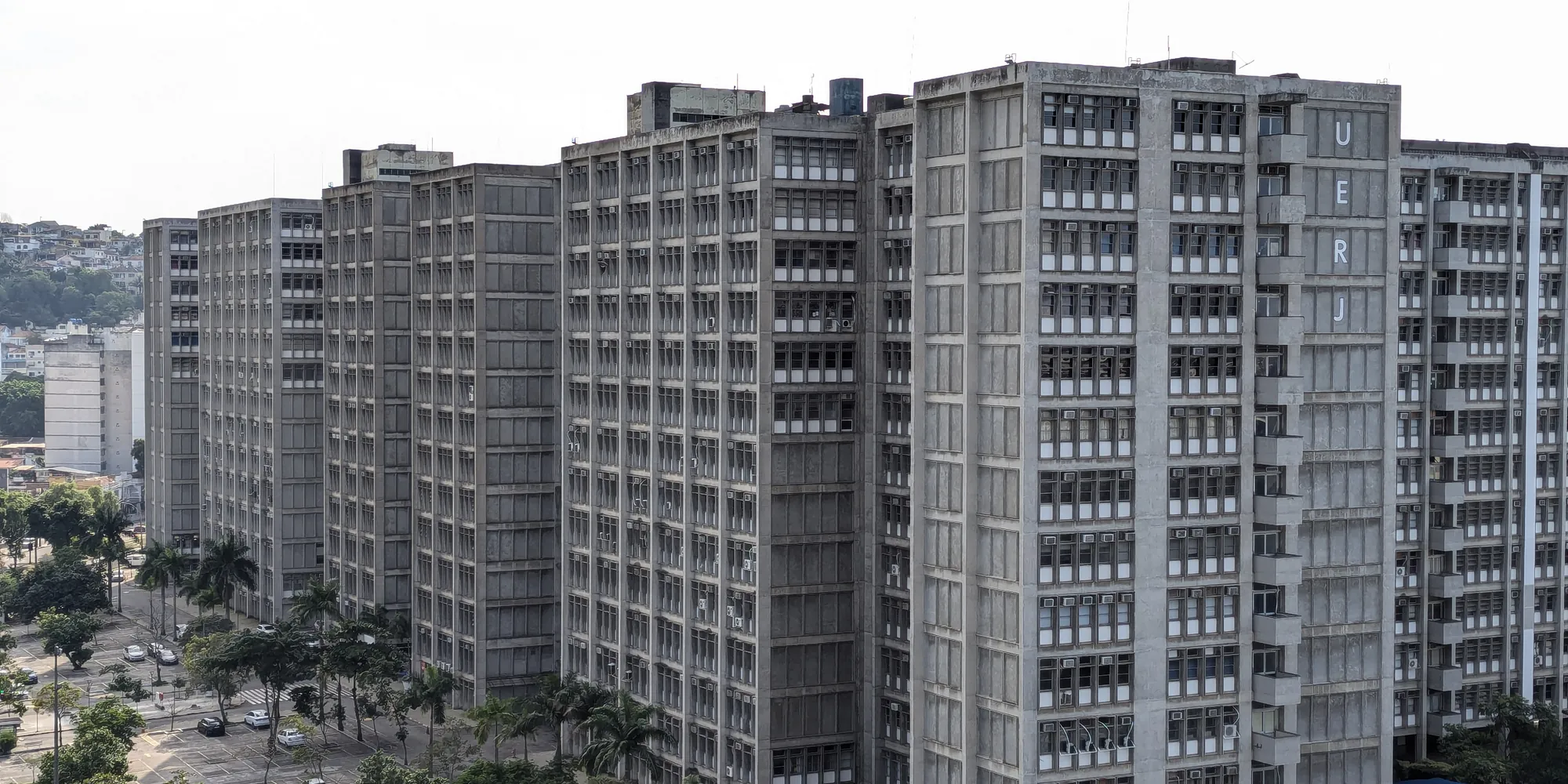 Vista aérea do campus Maracanã da UERJ, com o extenso bloco de concreto do Pavilhão Reitor João Lyra Filho atravessando o enquadramento, cercado pela cidade.